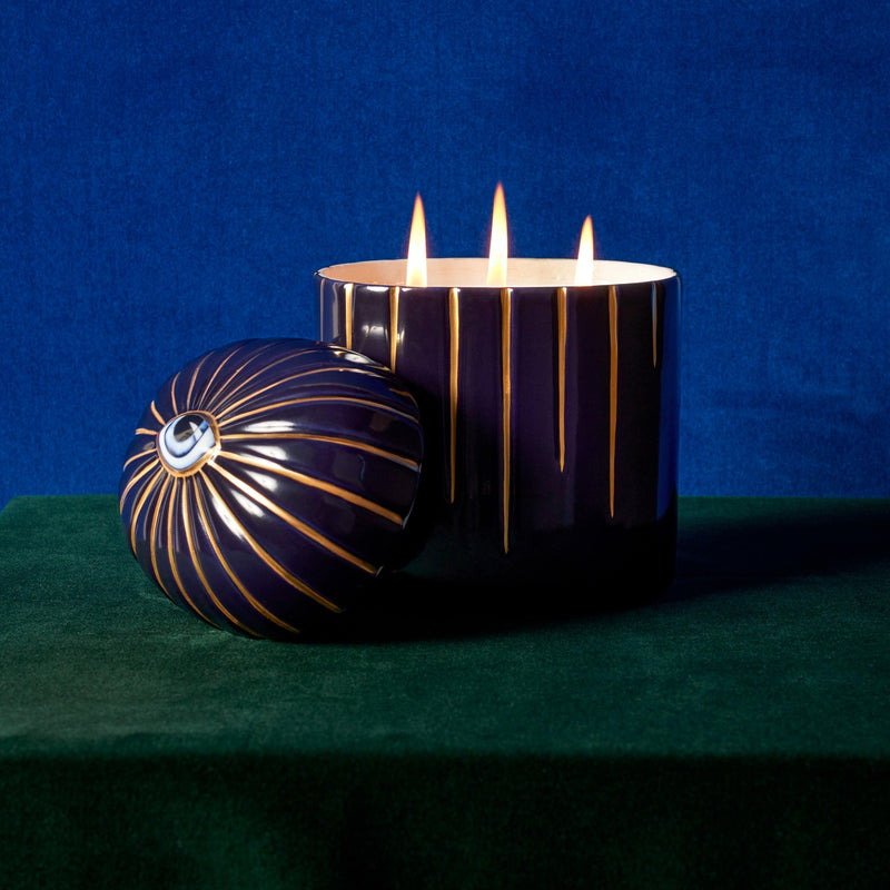 Lito Candle 3-wick Blue  with eye motif posed with a moody royal blue and emerald green background