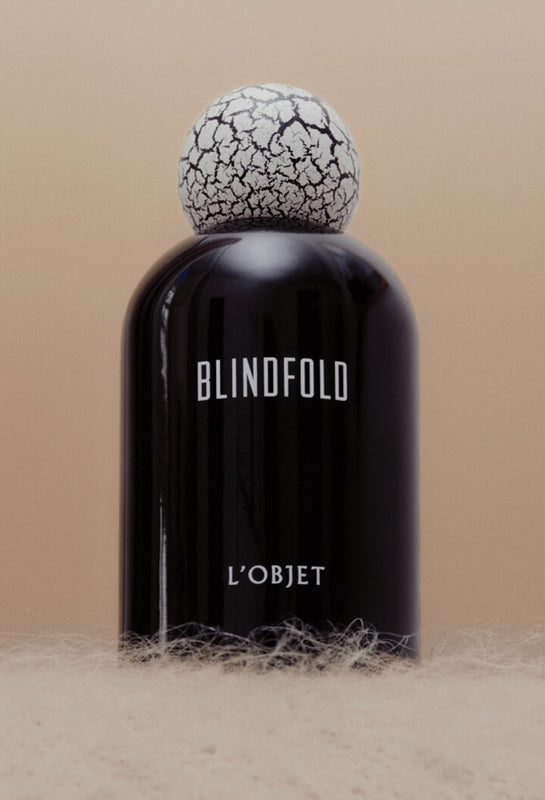 Black bottle with cracked white cap labeled 'Blindfold' by 'L'Objet' on a beige background