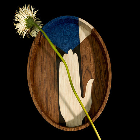 Discover the Edgar Collection. Mutlicolored Wooden Tray with Hand Motif on top of a flat black background. Cut flower placed on tray.