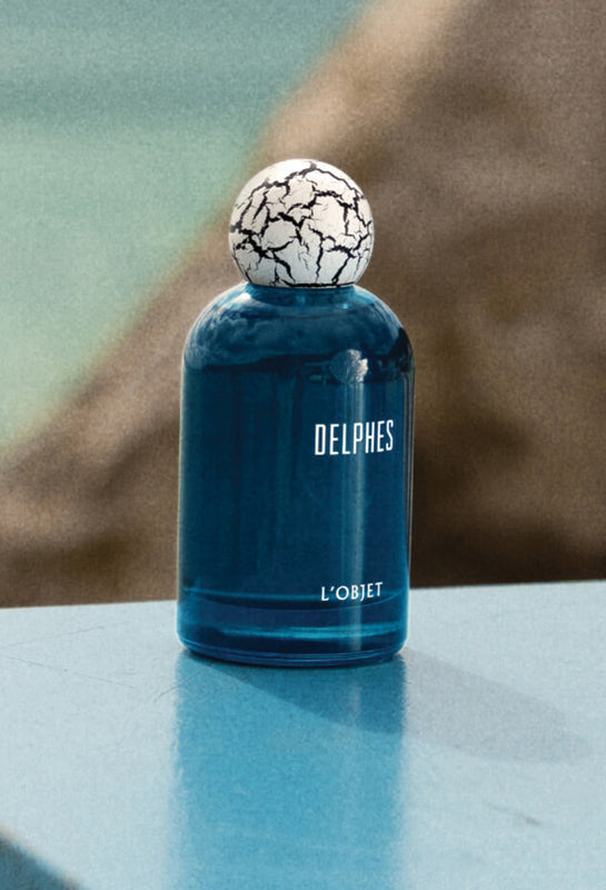 Blue perfume bottle with a cracked white cap on a reflective surface