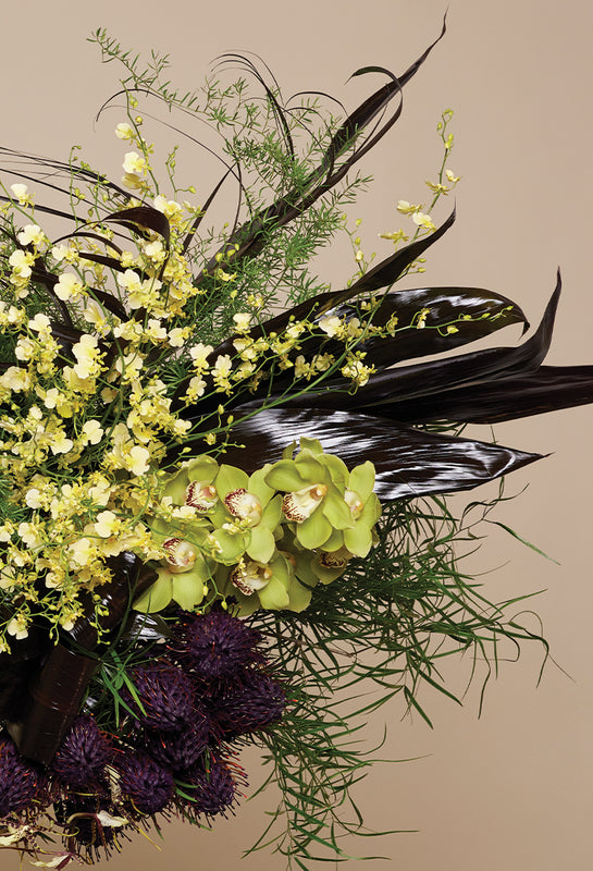 Floral arrangement with green orchids, purple thistles, and yellow flowers on a beige background