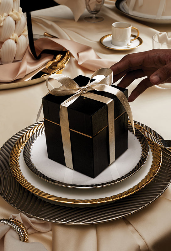 Black gift box with a white ribbon on a decorative table setting.