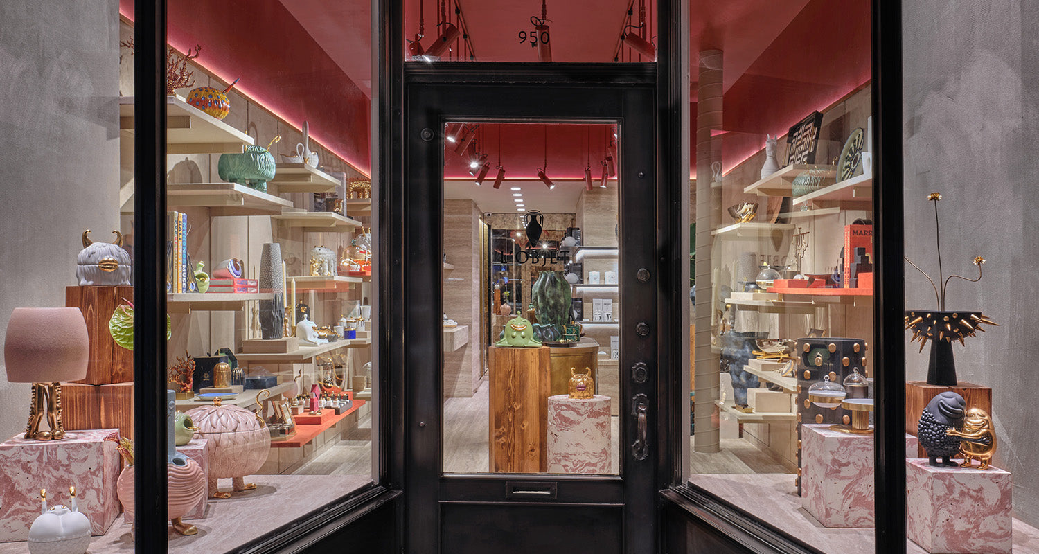 L'OBJET Madison Avenue, New York City Flagship. Image of exterior storefront with array of decor and dinnerware products arrange in long space with pink and white marble cubes and shelves. Colorful and wooden interior design. 