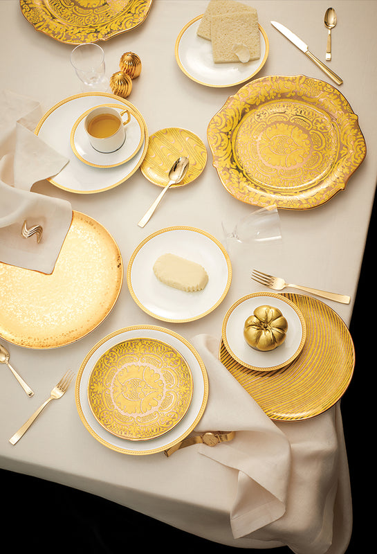 Elegant table setting with gold plates, silverware, and white napkins on a beige tablecloth.