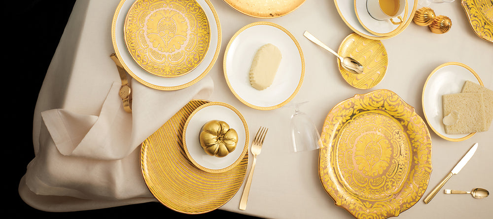 Gold and white table setting with decorative plates and cutlery on a white tablecloth.