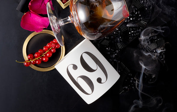 Porcleain candle vessel labeled with the number 69 scattered with lipstock stained cognac glass and rose petals