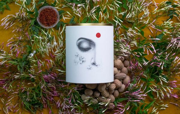 Porcelain candle vessel with illustrated woman's face in a bed of jasmin and saffron