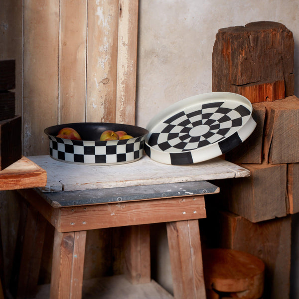 Black and white checkerboard glaze pattern on a low, round porcelain platter and flared bowl.