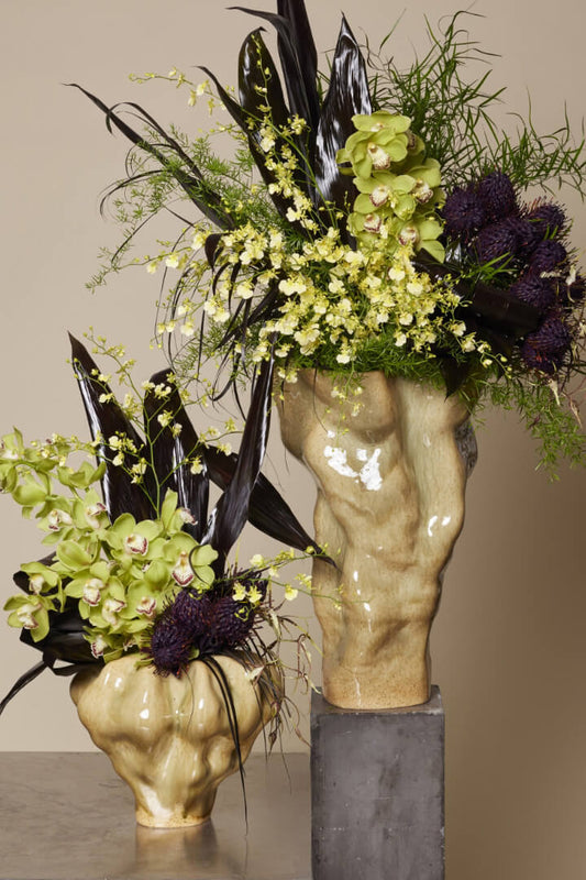Decorative flower arrangement in a sculpture-like vase on a neutral background