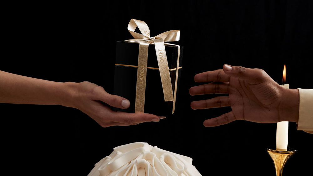 Two hands exchanging a gift box with a gold ribbon against a dark background.
