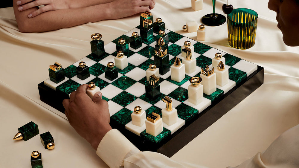 Two people playing a game of chess with green and white pieces on a checkered board.