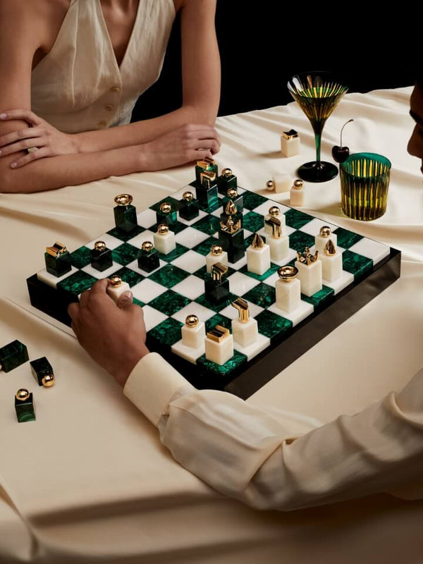 Two people playing a game of chess with decorative pieces on a checkered board.