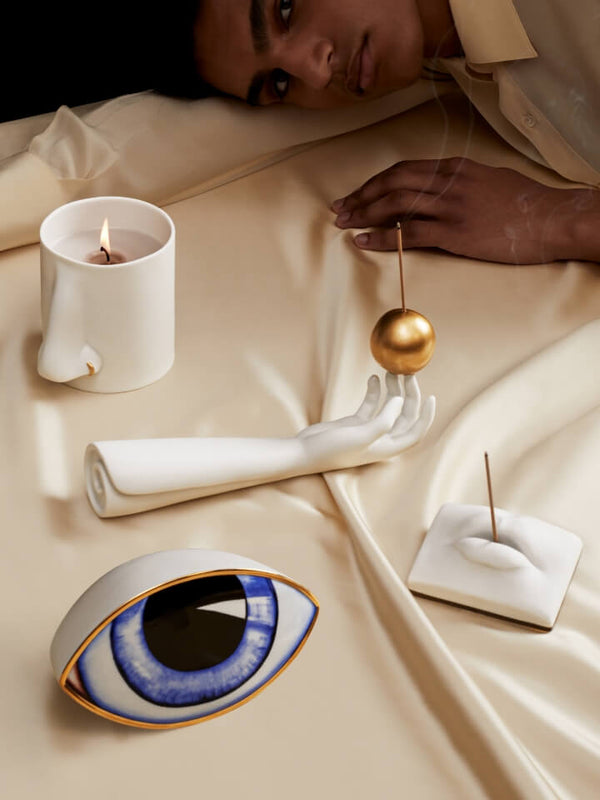 Decorative items including a candle, eye-shaped object, and hand-shaped holder on a beige fabric surface.