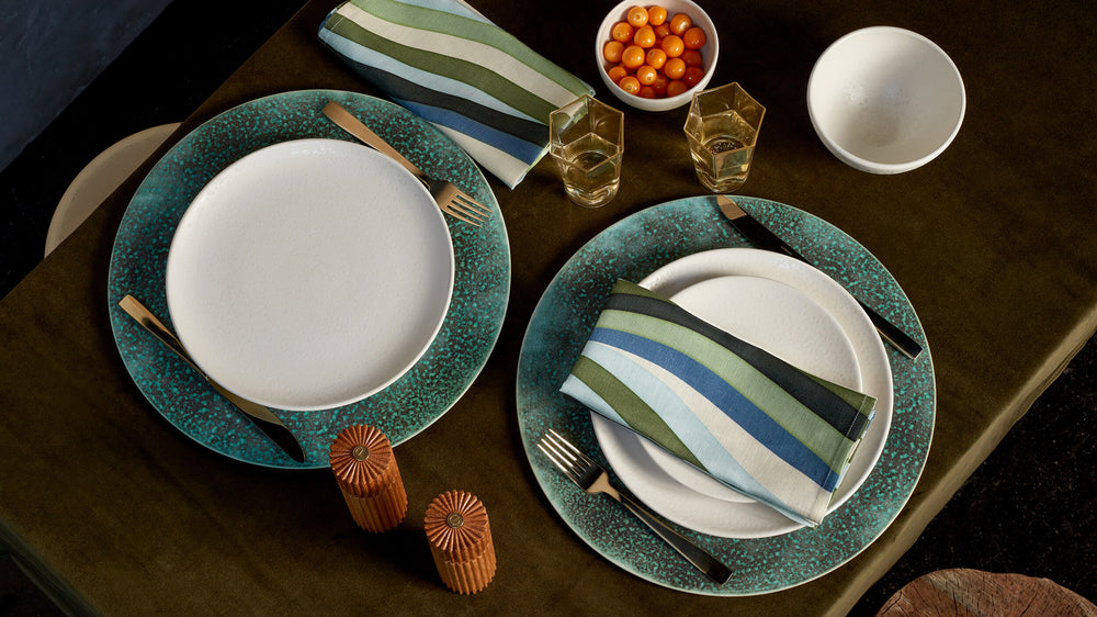 Shop Dinnerware and Table Accents. Colorful sea colors chargers and printed napkins with white porcelain plates, textured wooden table and wooden salt and pepper shackers. gold rectangular glassware and ground berries in a white bowl. 