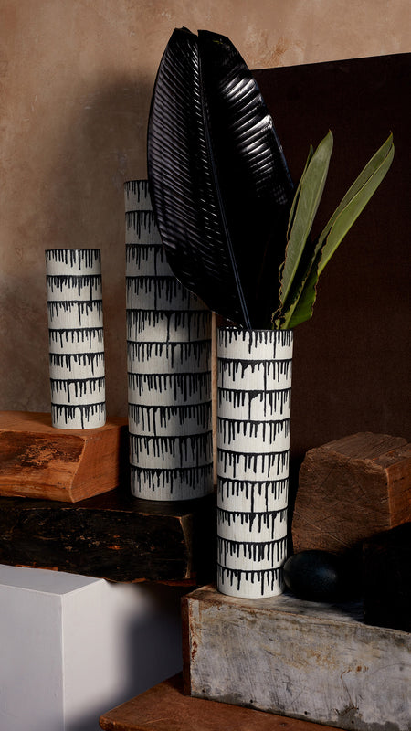 Discover New Arrivals. Vases and Bowls in white texture with indigo dripping glaze sitting on blocks of wood in front of a washed beige wall and taupe suede curtain. 