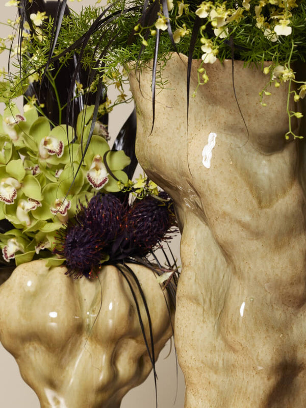 Two flower arrangements in unique vases against a plain background