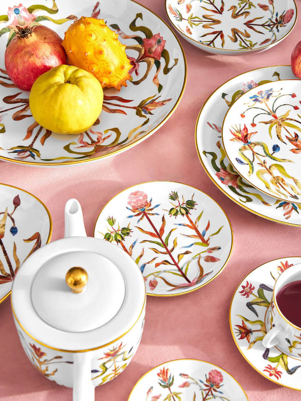 Decorative ceramic plates with floral patterns on a pink surface, featuring a teapot and cup.
