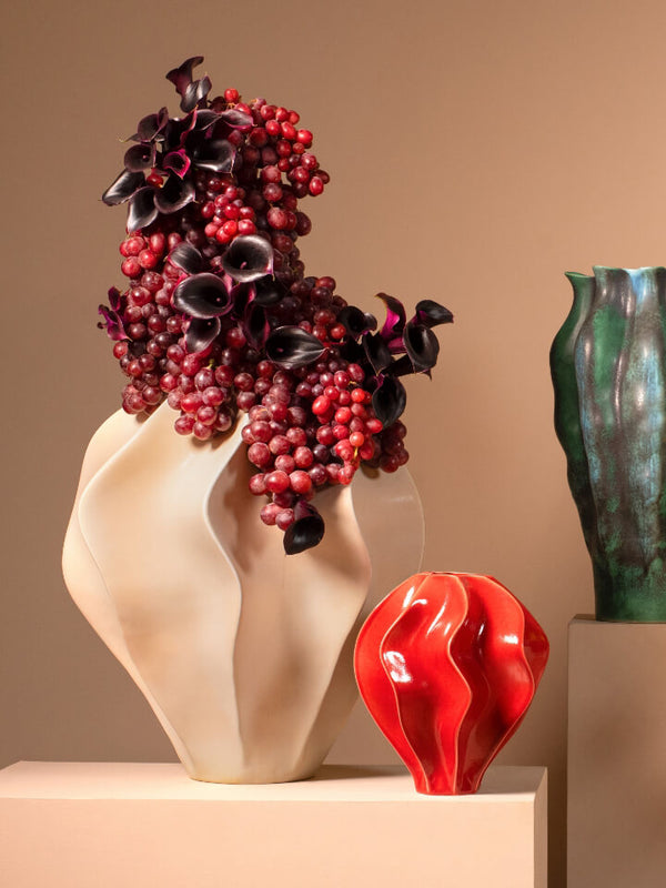 Decorative vase with red and black floral arrangement on a beige surface with a brown background