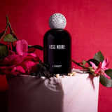 black bell shaped glass bottle with round crackle top styled with a moody red background and rose 