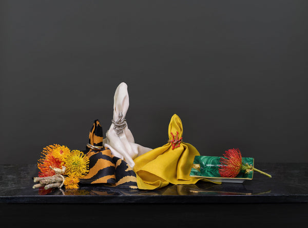 Group of L'Objet linen napkins in ecru, mustard and organe tiger print with napkin jewels- bird, 3-ring, snake and coral. Malachite pattern porcelain ashtray.